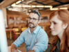 A man and a woman talk in front of the PC about work processes in onOffice.