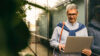 Man wearing glasses using a laptop in front of a modern glass building