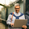Man wearing glasses using a laptop in front of a modern glass building