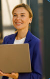 A smiling businesswoman in a blue blazer is holding a laptop